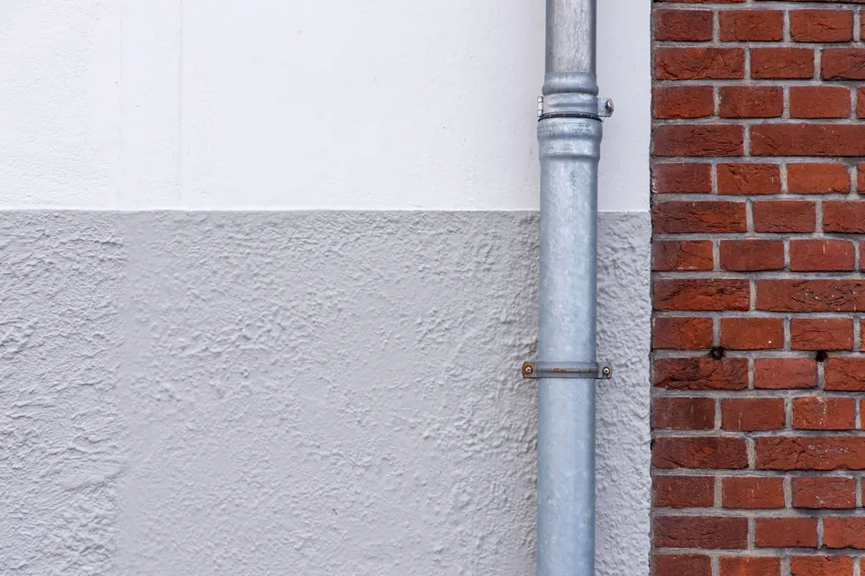 Tuyau de descente en acier galvanisé entre un mur enduit et un mur de briques