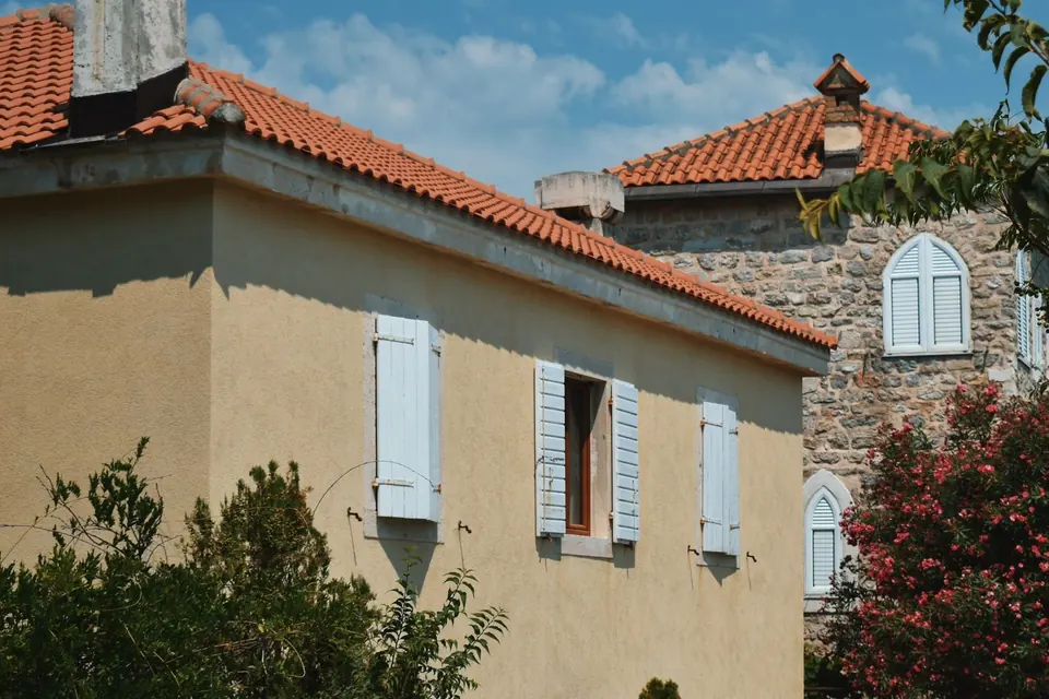 Maison à enduit clair et volets, toiture en tuiles de terre cuite, maison en pierre à l'arrière