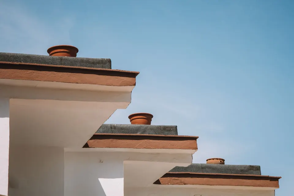 Toits plats étagés d'une maison blanche, rives soulignées de terre cuite